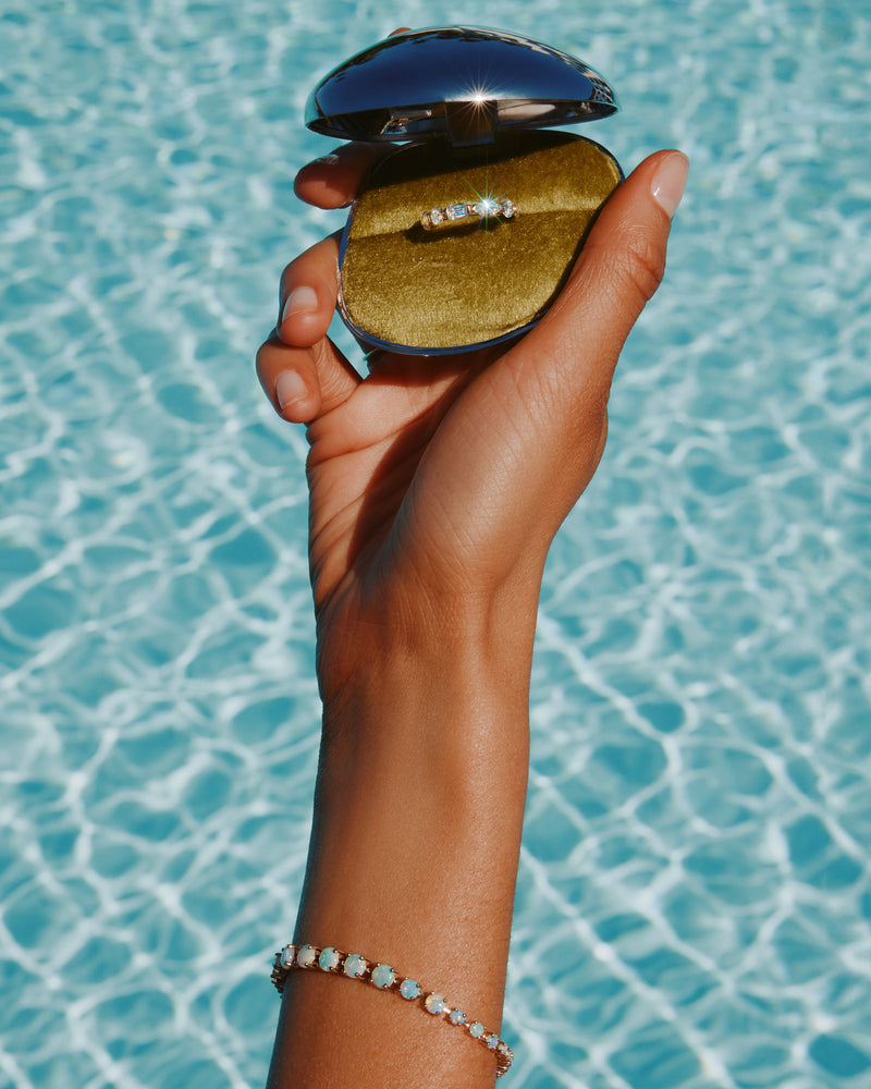 Hand holding a clamshell jewellery box with a ring against a pool background